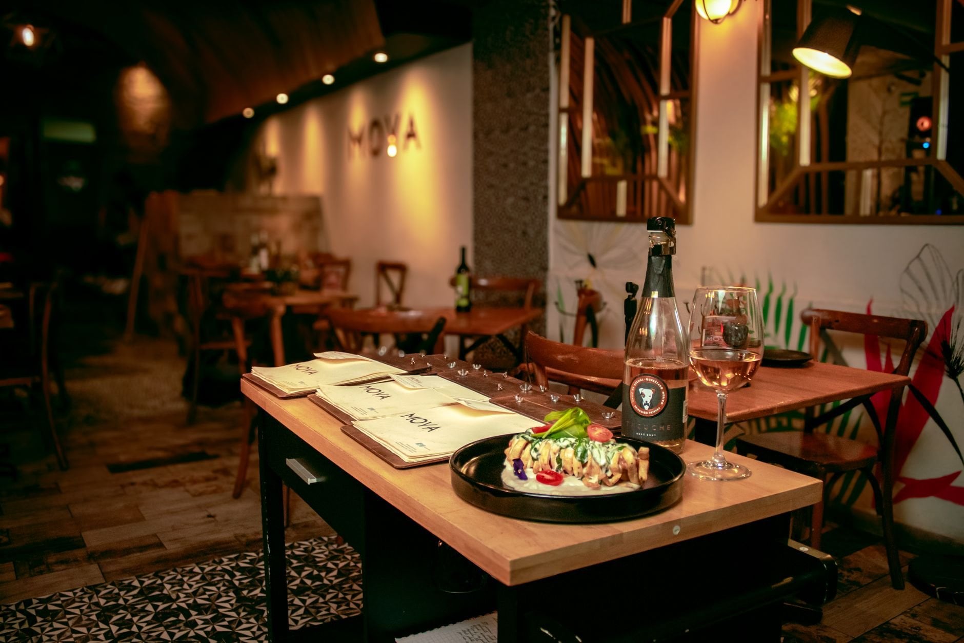 Cosy restaurant table with a plated dish and wine in warm light.